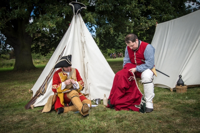 Soldiers in period costume outside tent, sewing.