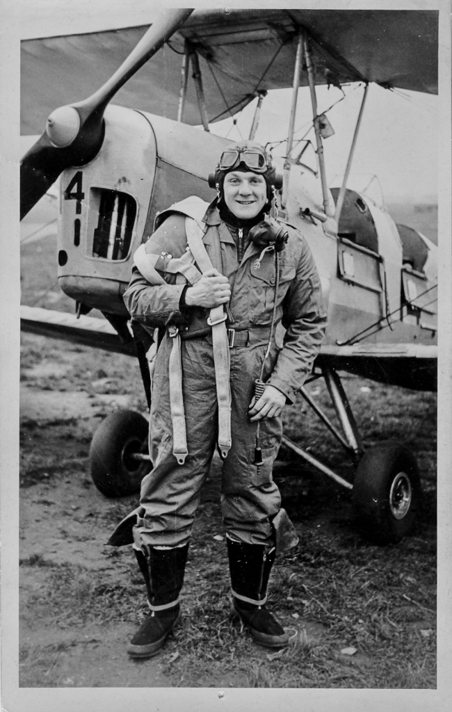 Young man in fliying gear standing in front of a biplane.